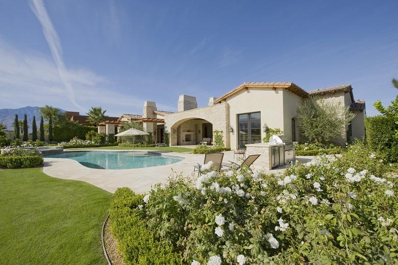 House exterior in daylight with a garden, plants, a swimming pool and hills in the far distance