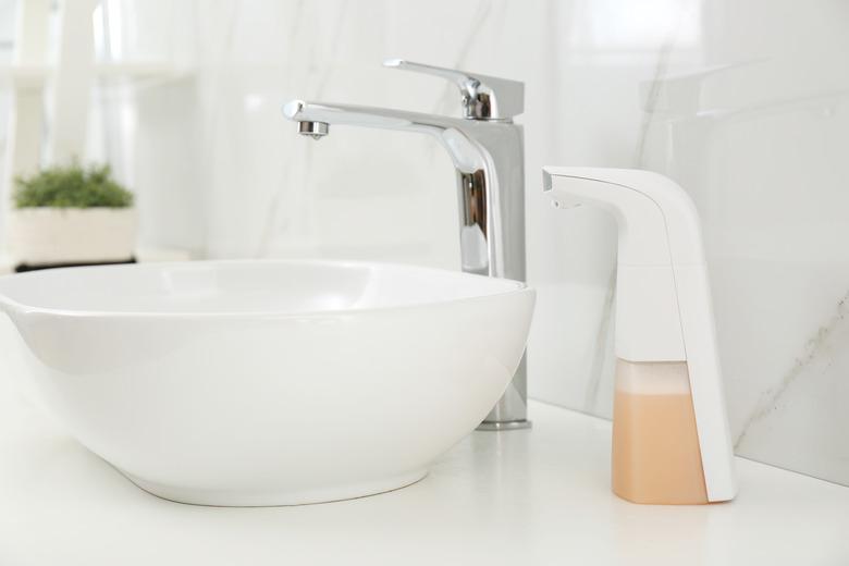 Modern automatic soap dispenser near sink in bathroom, closeup