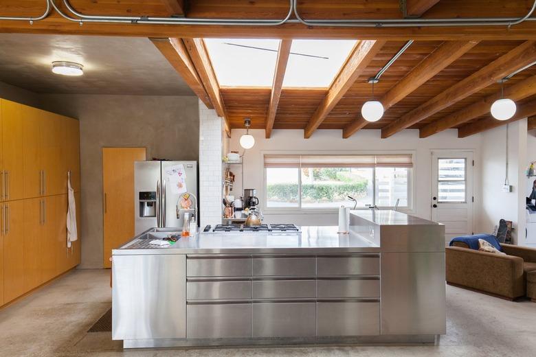 Industrial kitchen with a wood ceiling, skylights, globe pendant lights, wood cabinets, and a metal or steel kitchen island.