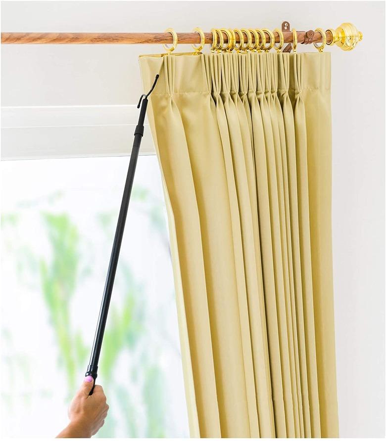 A woman using a curtain pull to draw the curtains closed