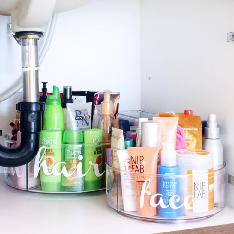 under sink storage with clear labeled containers with beauty products under bathroom sink