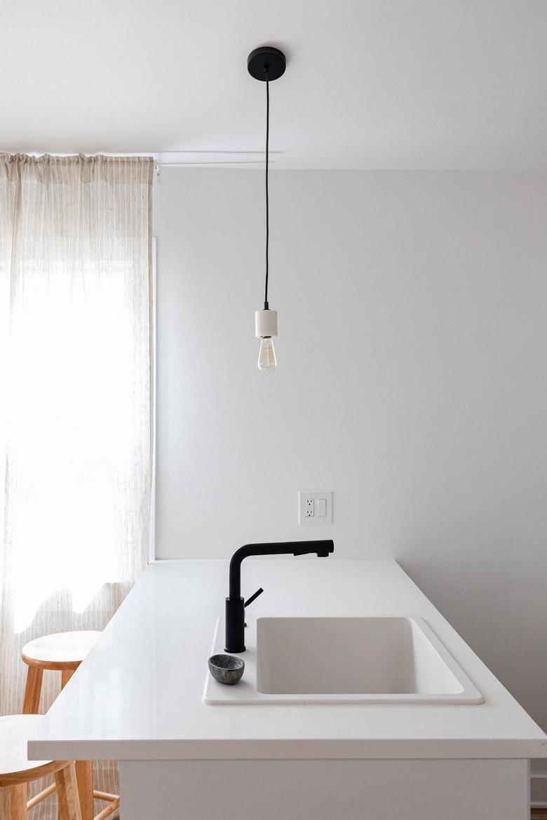 Minimalist white kitchen island with a black faucet and a lightbulb pendant light