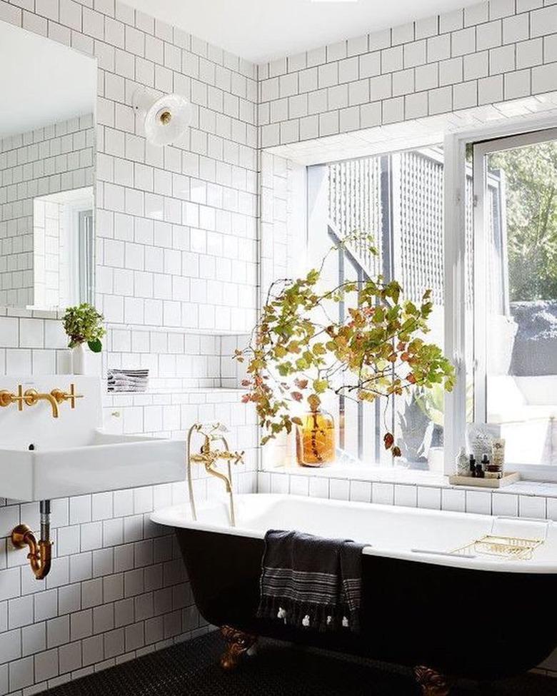 black clawfoot bathtub with brass fixtures and white subway tile