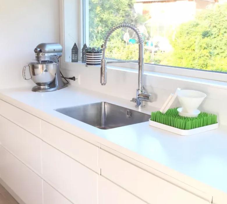 Best kitchen sink materials Stainless steel sink with stainless faucet, white counters, white cabinets, mixer, window.