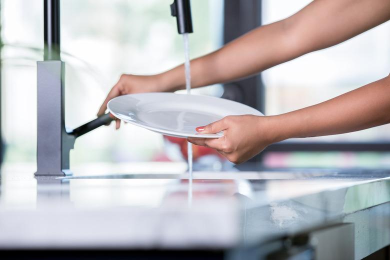 Young woman rinses plate while standing at kitchen sink and washing dishes