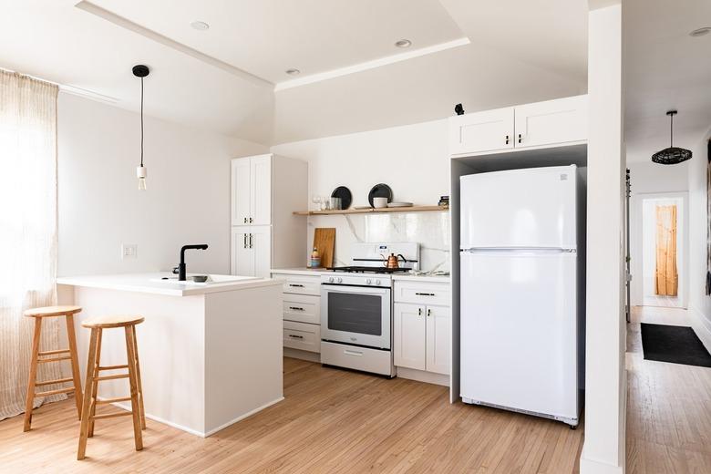 Minimalist kitchen with white walls and cabinets, wood floors and black accents