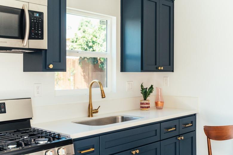 Kitchen with dark cabinets with gold handles and white countertop with single-handle kitchen faucet and a houseplant