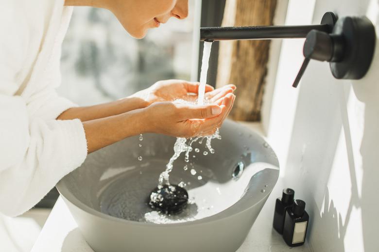 Young woman awakening, washing and cleaning her face with splashing water. Unrecognisable person