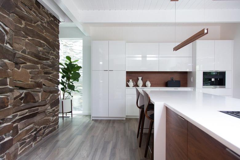 A stone wall and gray floor, in a Minimalist kitchen with white cabinets and a bar pendant light.