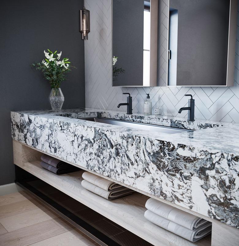 thick slab quartz bathroom countertop with black faucets and chevron wall tile