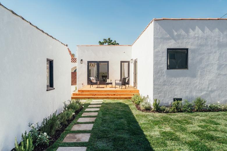 Backyard area with grass, concrete pavers, and wood deck with outdoor furniture.