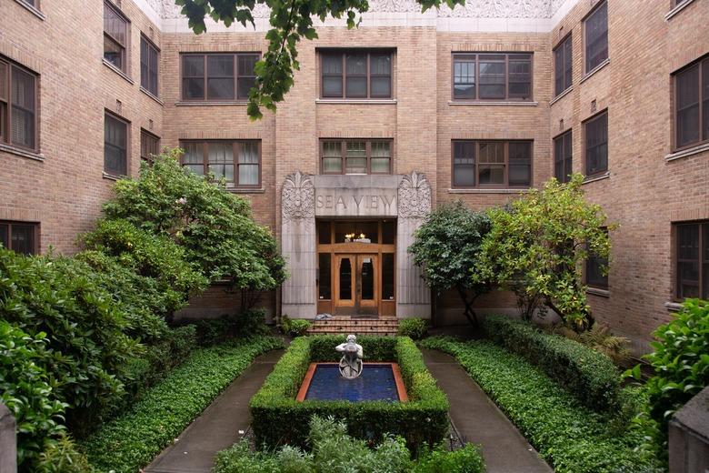 A courtyard of an apartment, with a fountain and lined with bushes.