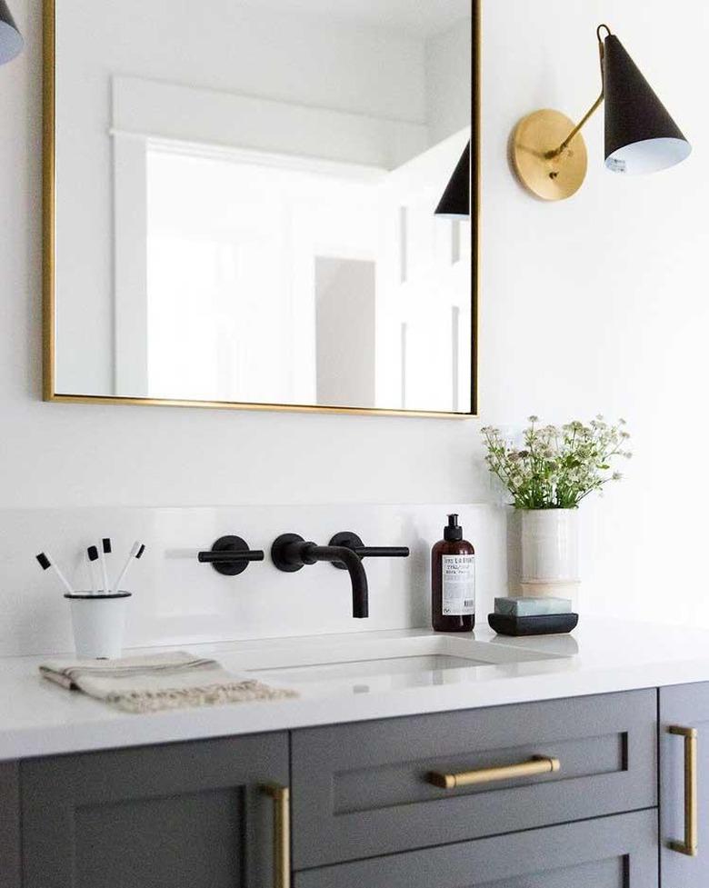 white bathroom countertop with gray cabinets and brass hardware and black fixtures