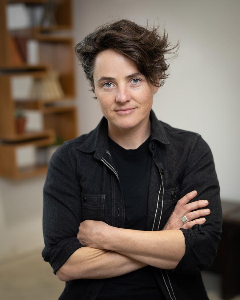 Furniture designer Alexis Moran standing, wearing a black button-down shirt over a black T-shirt with her arms crossed.