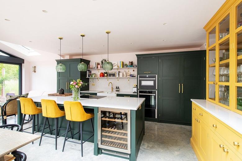 Kitchen with dark green cabinets and yellow barstools.