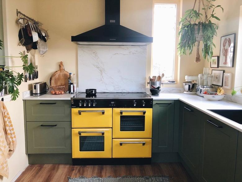 Bohemian kitchen with a yellow stove, green cabinets and hanging pots.