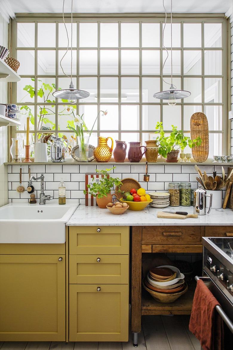 Eclectic kitchen with mustard yellow lower cabinets, a farmhouse sink and green plants.