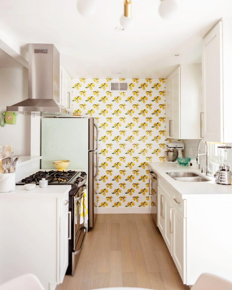 Small kitchen with white cabinets and lemon patterned wallpaper.