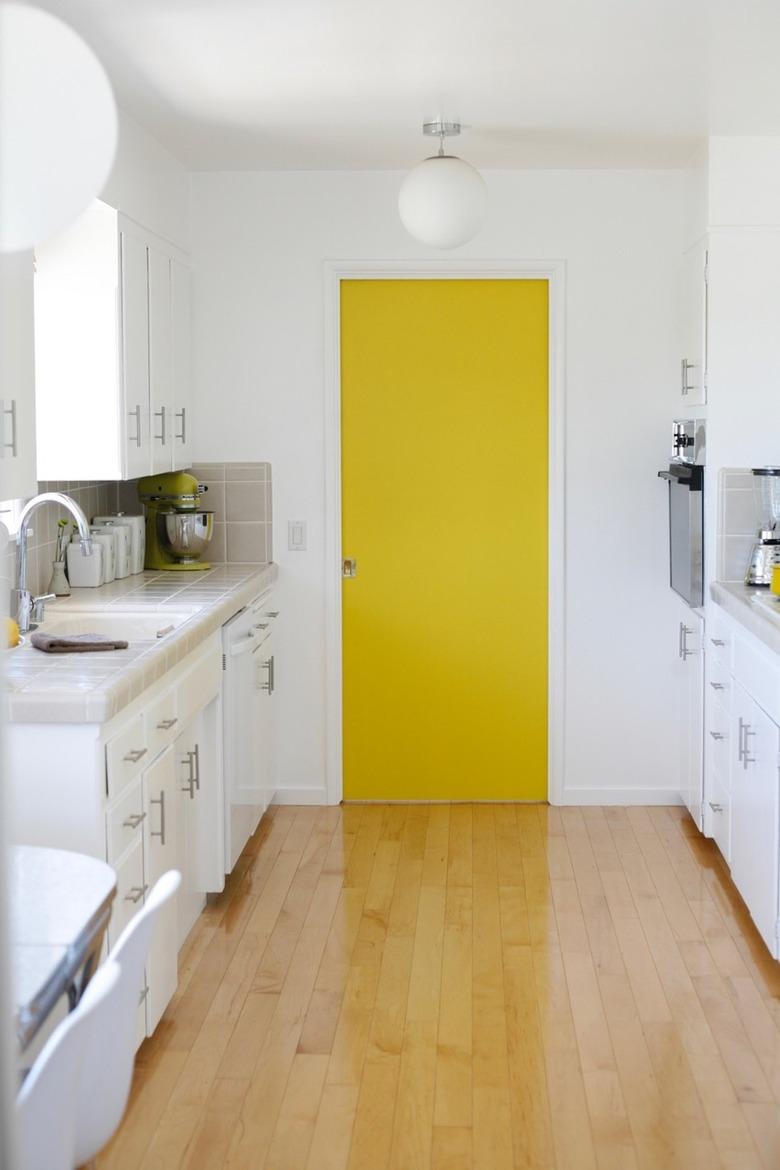 White minimalist kitchen with bright yellow pantry door.