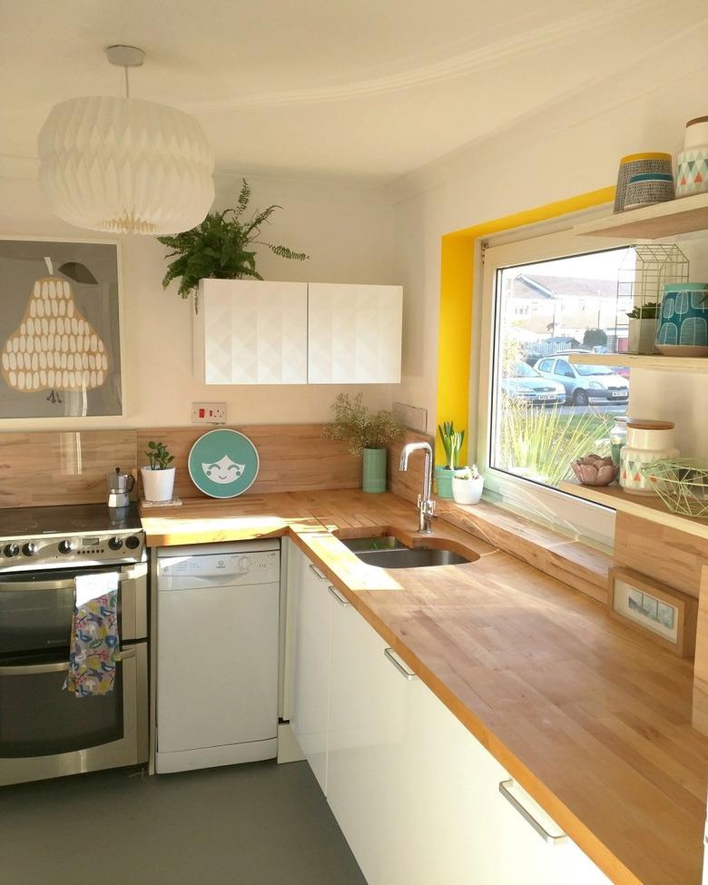 White minimalist kitchen with butcher block countertops and yellow window trim.