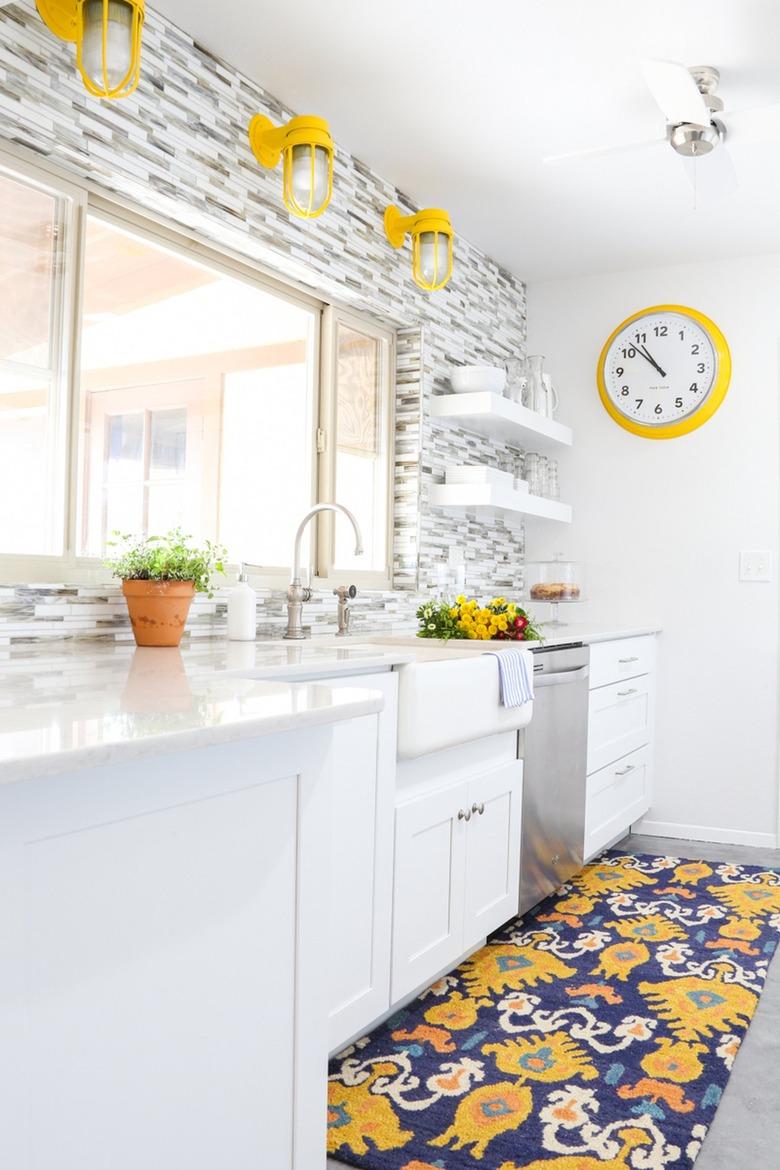 White kitchen with grey and white backsplash, a farmhouse sink and yellow industrial light fixtures.