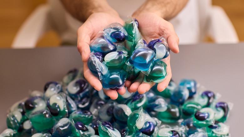 hands cupped together holding detergent pods above a pile of pods on a table