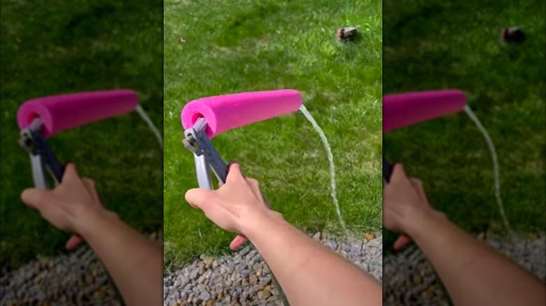 Hand holding hose nozzle with attached pool noodle extender, spraying water