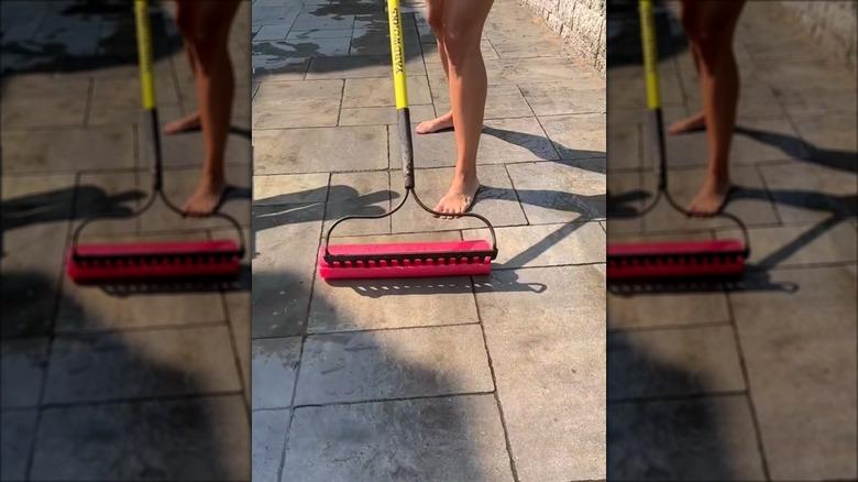 woman squeegeeing the patio using a pool noodle on a garden rake