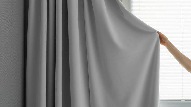 woman holding up a side of a solid gray drapery panel hung beside a window