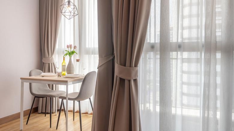 A small dining nook with white walls and taupe curtains.