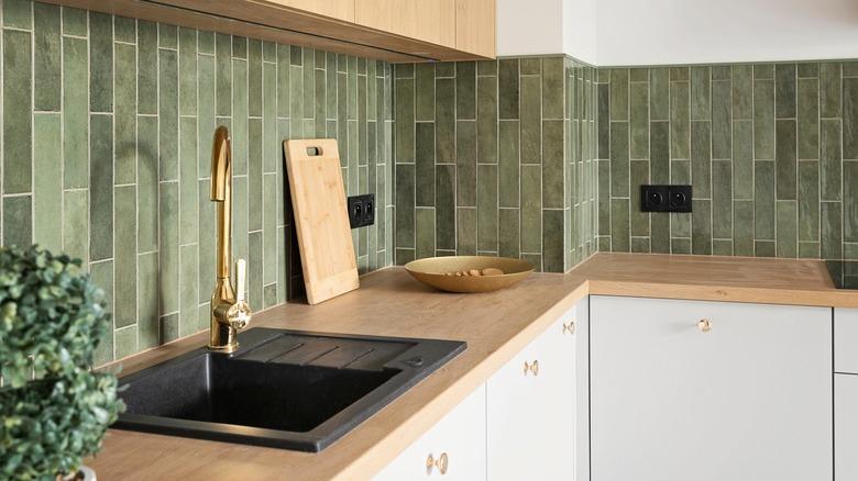 kitchen with white cabinets, light wood countertops, gold faucet, black sink, and an olive green vertical subway tile backsplash