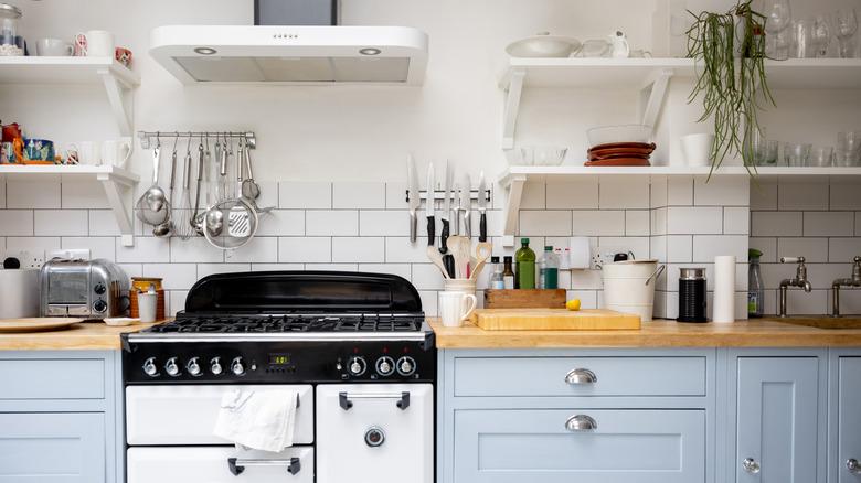 kitchen with light blue cabinets, light wood countertops, vintage black and white stove, white subway tile, and open upper shelving