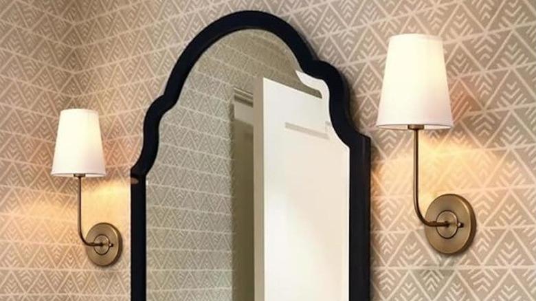 gold sconces with white shade around mirror