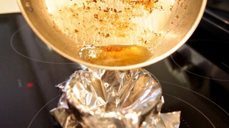Pouring bacon grease from pan into aluminum foil bowl