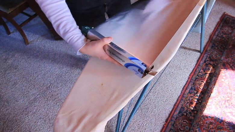 Rolling sheet of aluminum foil onto ironing board