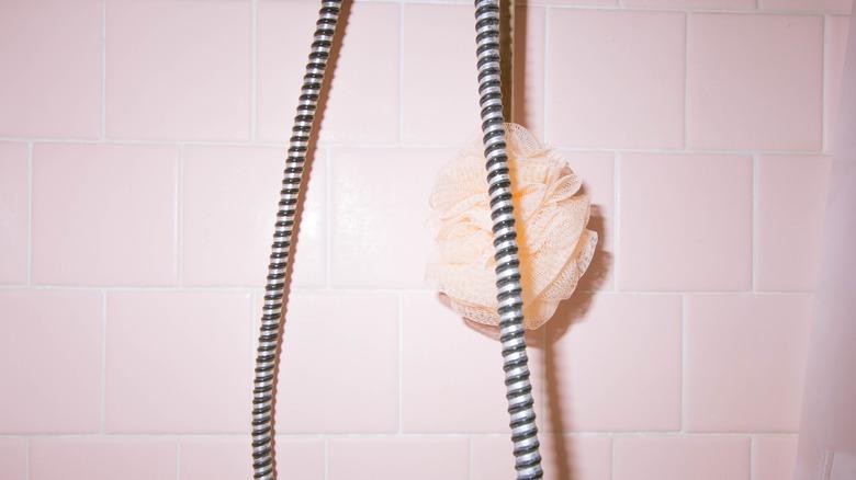 light pink tile with a pink loofah and the cord of a handheld showerhead