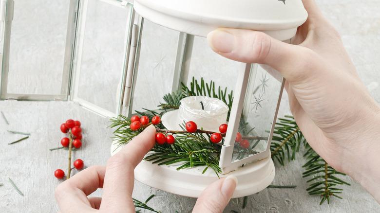 white lantern with greenery, candle, and holly berries