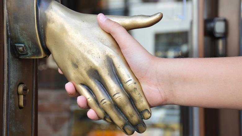 brass door knob shaped as a hand extended for a handshake with a human hand operating it