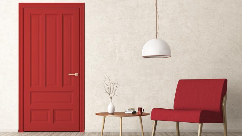 red interior door wtih plain walls, red chair, lighting, and small side table with deco