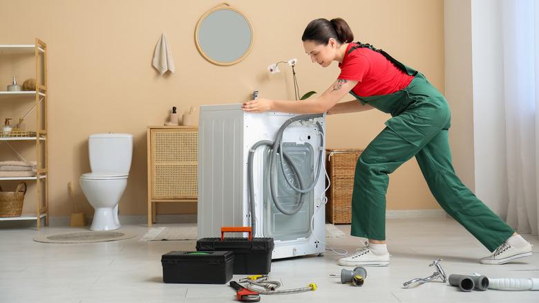 Woman moving a washing machine across a bathroom