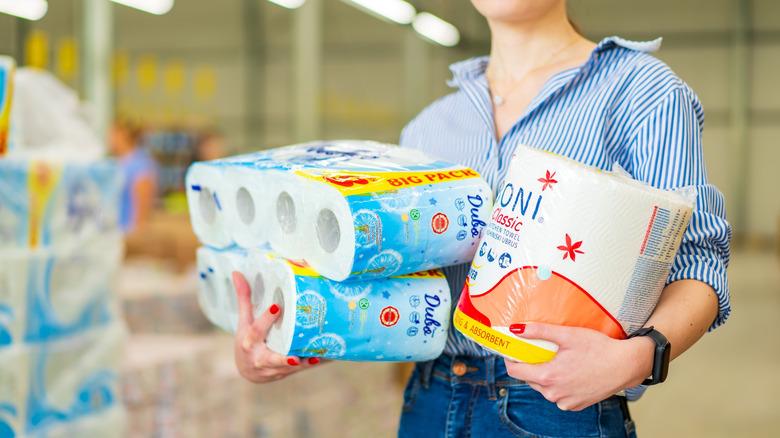 Person holding packaged paper towels and toilet paper
