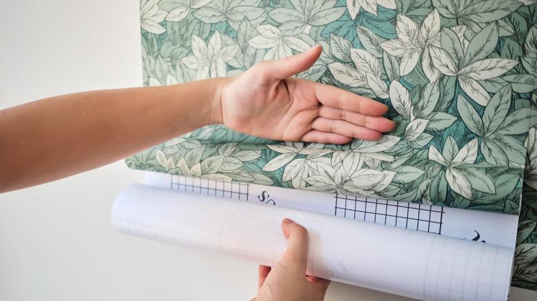 hand smoothing green leaf peel and stick wallpaper onto wall