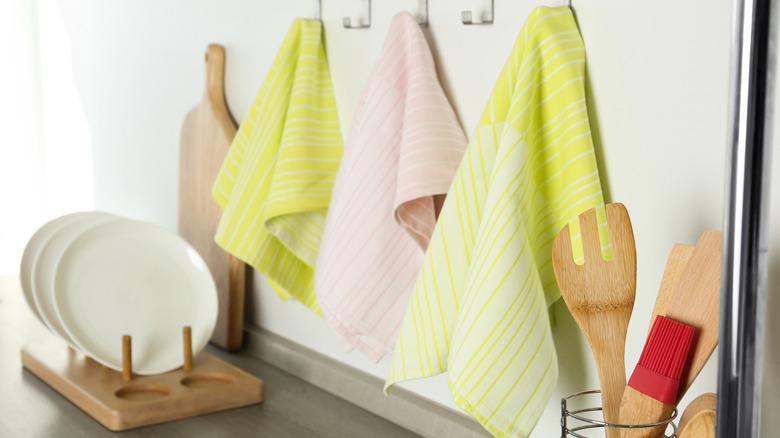 dish towels hanging from a hook, dishes sitting in a dish rack, kitchen utensils visible in background