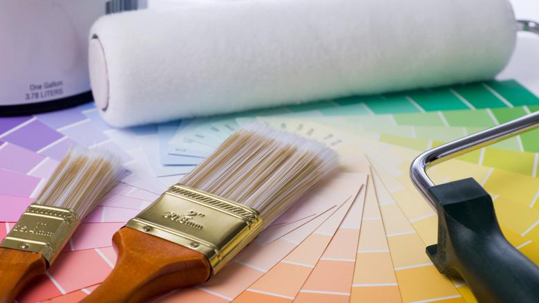 two paint brushes and a white paint roller on a stack of colorful paint samples