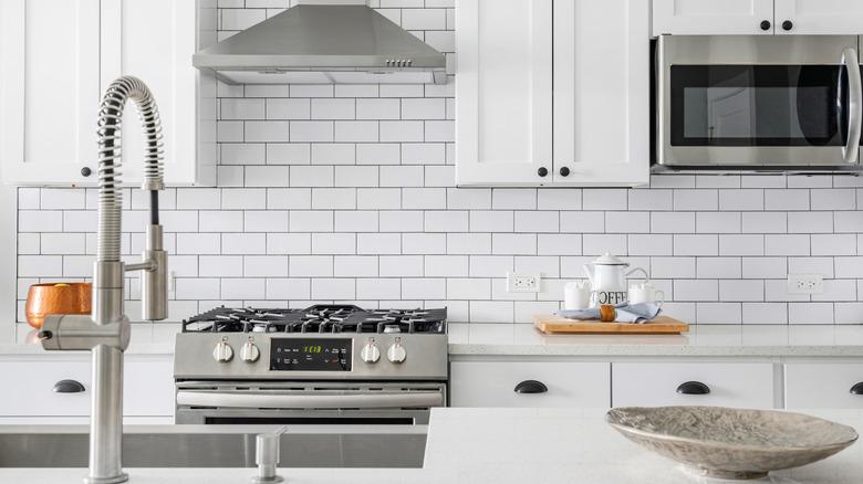 A bland kitchen with white cabinets, black hardware, white counters, white subway tile, stainless steel appliances and plumbing fixtures