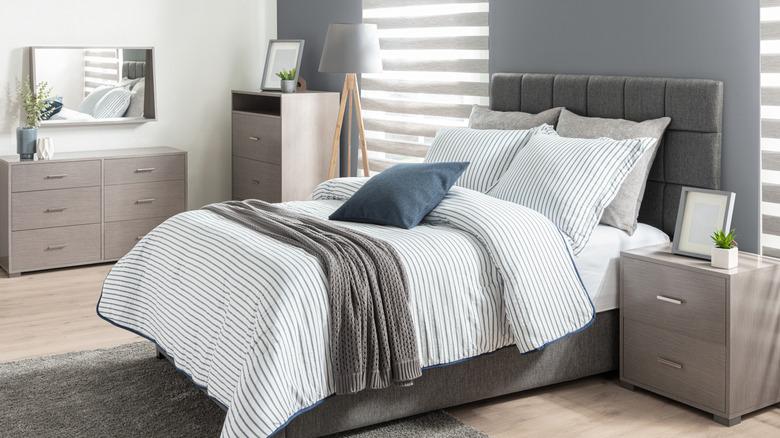 A boring bedroom with a gray accent wall, greige matching bedroom furniture set, gray tufted headboard, and white pinstripe bedding