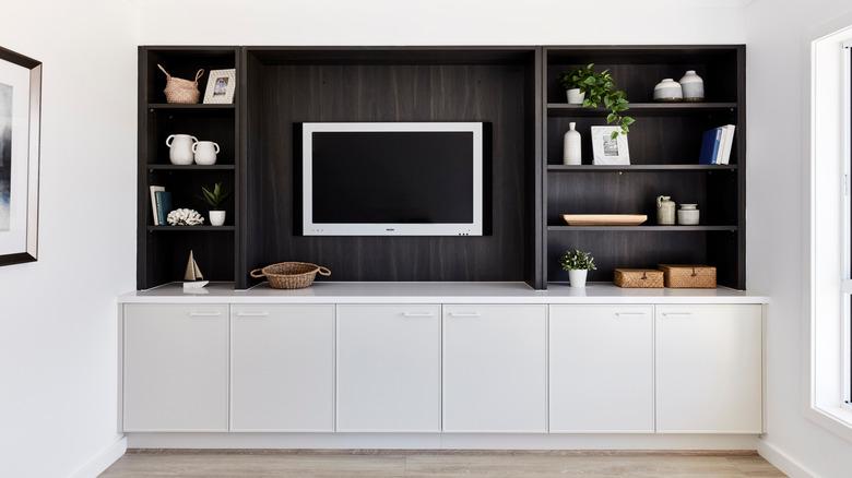 modern living room built-in cabinets with light gray lower cabinets, a dark wood upper backdrop, and dark wood upper shelves around a TV