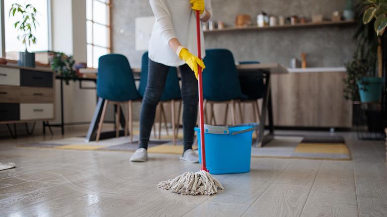 woman mopping kitchen floor with bucket of water nearby