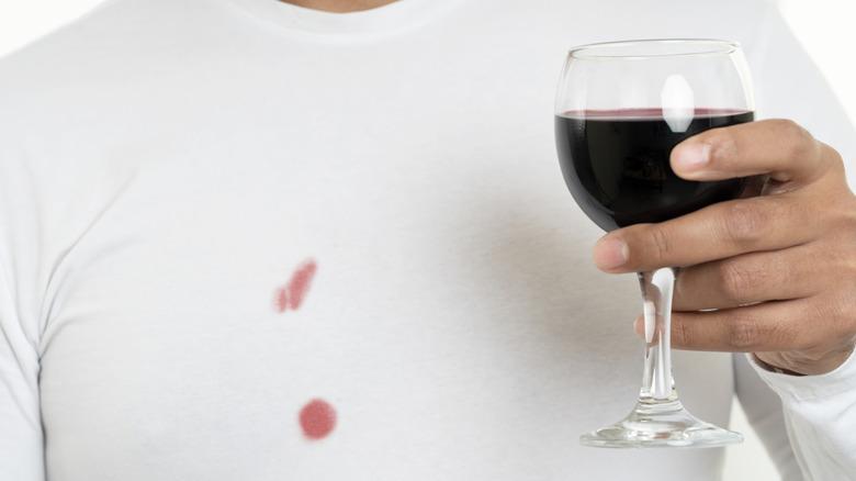 Man holding glass of red wine with stains on shirt