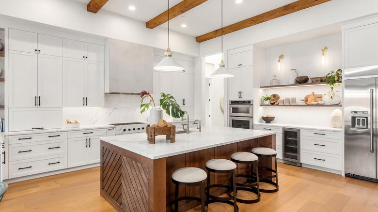 modern kitchen with white cabinets that extend all the way to the tray ceiling, which has exposed wooden beams